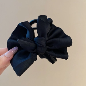 Detail of a black fabric bow hair claw clip with a glossy satin finish and secure grip