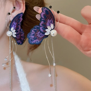 Detail of purple embroidered butterfly earrings with pearl accents and long metal tassels