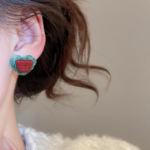 Close-up of model wearing green fabric heart earring with a small red bear charm