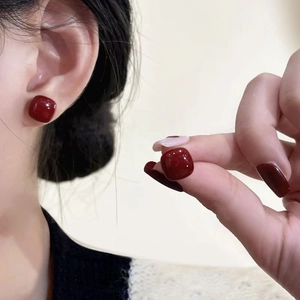 Close-up of elegant square red pearl stud earrings worn on ear with high gloss finish