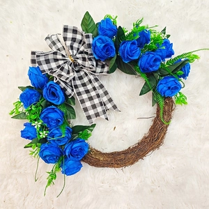 Blue rose Christmas wreath with green leaves and black-white buffalo plaid bow on rattan