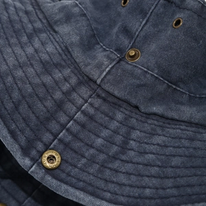 Détail macro du chapeau bob en toile lavée bleu marine avec coutures et œillets laiton