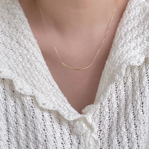 Close-up of minimalist gold curved bar pendant necklace on collarbone with white lace