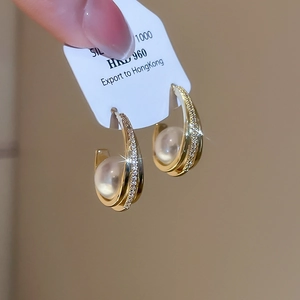 Detailed close-up of C-shaped 18K gold earrings with pearls and micro-set zircons