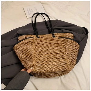 Detail of a large straw tote bag featuring contrast black handles on a soft fabric backdrop