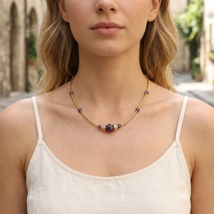 Close-up of a beaded gold necklace with purple amethyst stones worn by a model