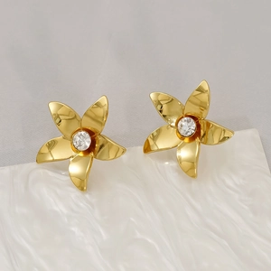 Polished gold floral stud earrings with crystal centers on a white textured stand