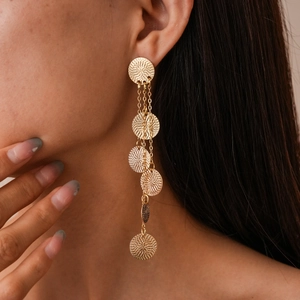 Close-up of elegant gold tassel earrings with circular textures worn by a model