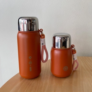 Detail of matte orange 316 stainless steel vacuum flasks with steel lids and carry ropes