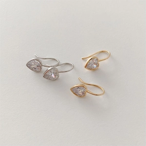 Macro detail of silver and gold heart-shaped zircon earrings with slender hooks