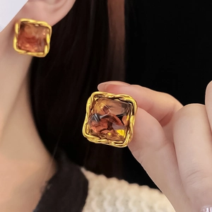 Detail of amber resin earring with twisted gold metal frame worn by a model