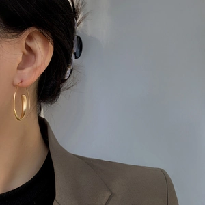 Detail of matte gold irregular geometric hoop earrings worn by a model in a suit