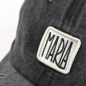 Makroaufnahme des bestickten 'MARIA'-Patches auf der gewaschenen grauen Baseballkappe