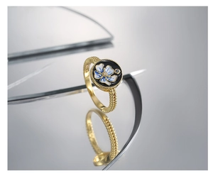 Close-up of golden floral enamel ring featuring blue lotus on black background and textured band