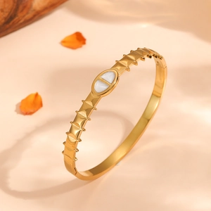 Close-up of a serrated titanium steel gold bracelet featuring a white oval oil-drop detail.