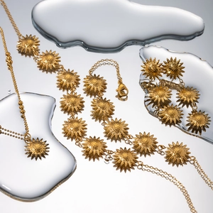 Detail of 18k gold stainless steel sunflower necklace and earrings set on reflective water