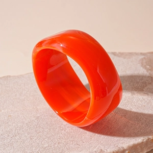 Detailed view of an orange translucent acrylic wide bangle on a textured stone base