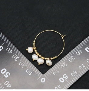 Macro shot of 40mm gold hoop earrings with white pearls and beads on black fabric