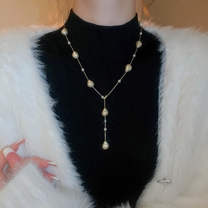 Detail of a gold-plated Y-shaped necklace with pearls on a black sweater backdrop