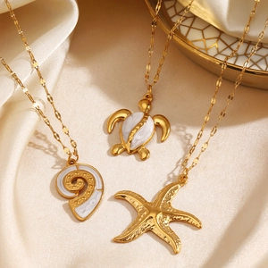 Golden starfish and turtle pendant necklaces on silk background for beach vacation style