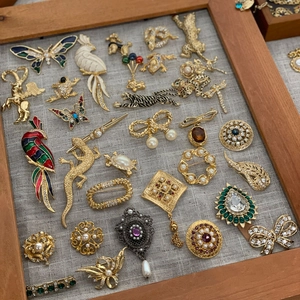 Vintage gold metal brooches with pearls and enamel displayed in a wooden tray