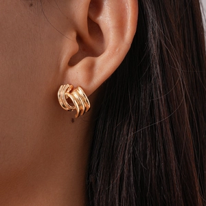 Macro shot of gold geometric C-shaped hoop earrings worn by a model in a minimalist style