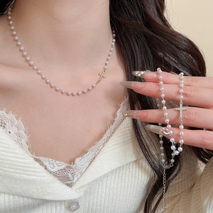 Close-up of French style pearl necklace with cross pendant on lace knit top