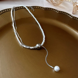 Detail of silver double-layer necklace with white pearls and square charms on vintage plate