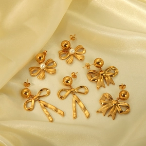 Close-up of golden bow earrings with white pearl accents on elegant silk background