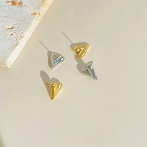 Flat lay of gold and silver chunky heart-shaped stud earrings on a beige stone background