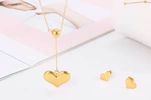 Flat lay of gold heart pendant necklace and earrings set on white background