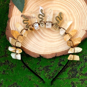 Detail of a raw quartz crystal crown with brass snakes on a natural mossy wood base