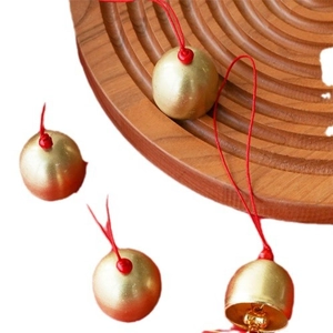 Golden metal wind chime bells with red hanging ropes on a textured wooden tray