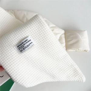 Close-up of white scarf with waffle knit texture, quilted fabric and woven label