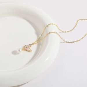 Collier plaqué or 14K avec pendentif papillon et perle blanche sur une assiette blanche
