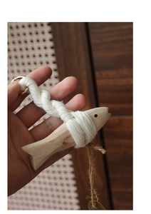 Detail of wooden fish hanging decor with white cotton weaving and golden metal ring