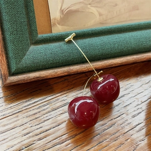 Detail view of red cherry earrings with gold stems placed on a rustic wooden table