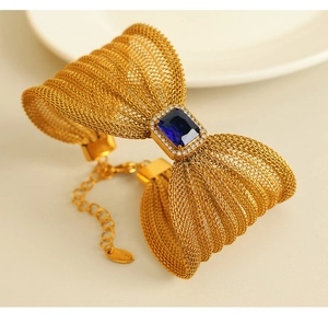 Detail of golden mesh bow bracelet featuring a central blue rectangular gemstone and small crystals
