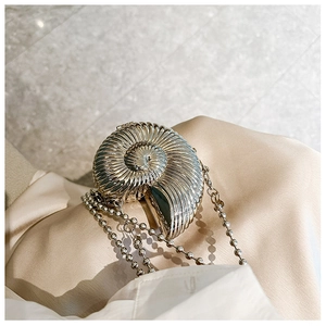 Macro shot of silver conch-shaped metal clutch bag with beaded chain on satin cloth