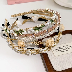 Détail de serre-têtes empilés avec perles, feuilles dorées et cristaux sur fond blanc