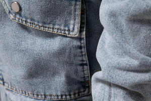 Macro shot of light blue denim jacket with yellow contrast stitching and metal button detail