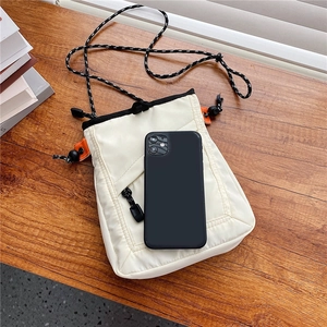White mini canvas crossbody bag with drawstring strap on wood desk with phone
