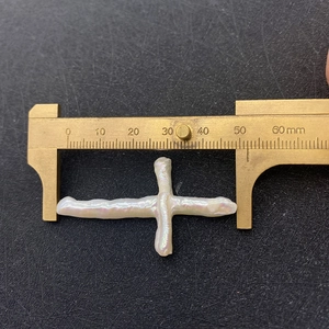 Macro shot measuring large white baroque pearl cross bead with brass caliper