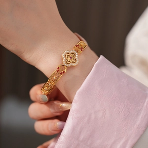 Close-up of vintage gold bangle with pearl and red gemstone in clover floral design