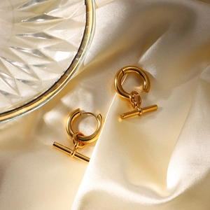 Detailed close-up of golden T-bar hoop earrings resting on elegant cream silk fabric