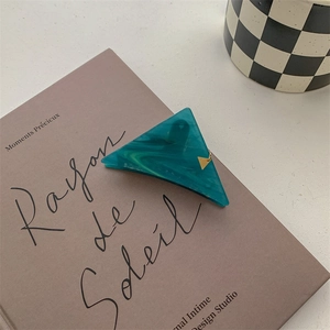 Detail of teal marble triangle hair claw clip with gold accent on a vintage book