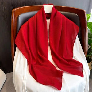 Detail of red cotton linen scarf draped on wood chair with soft fabric texture