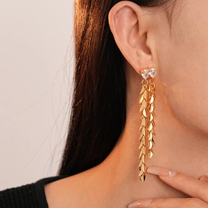 Macro view of gold leaf tassel earrings with heart-shaped zircon studs on a model