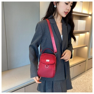 Detail of red nylon crossbody bag featuring front zipper pocket and metal ring decoration
