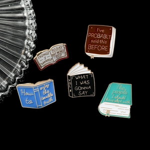 Detailed view of book-shaped enamel pins with creative English quotes on black background